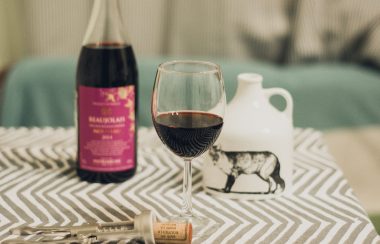 Une table sur laquelle on vois une bouteille de vin ouverte, un verre de vin est posé à coté, ainsi que le tire bouchon qui a servi à ouvrir la bouteille.