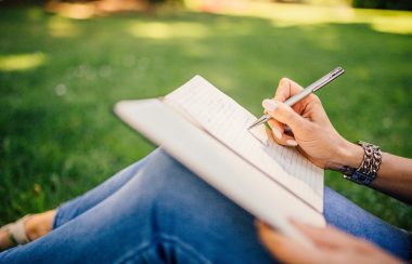 femme en jeans assise dans l'herbe qui écrit dans un carnet