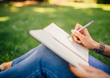 femme en jeans assise dans l'herbe qui écrit dans un carnet