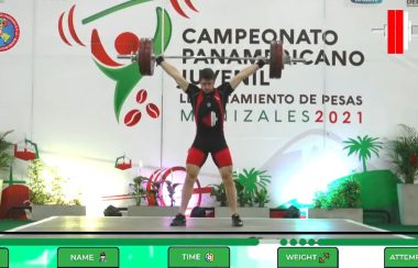 A photo of Xavier Lusignan competing at the Junior Pan American games, wearing a black and red singlet and lifting a barbell over his head.