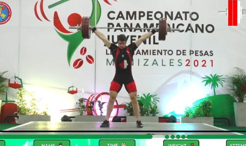 A photo of Xavier Lusignan competing at the Junior Pan American games, wearing a black and red singlet and lifting a barbell over his head.