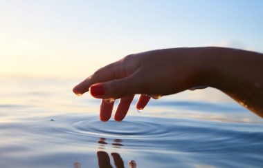 A hand stretches out to touch an expanse of water