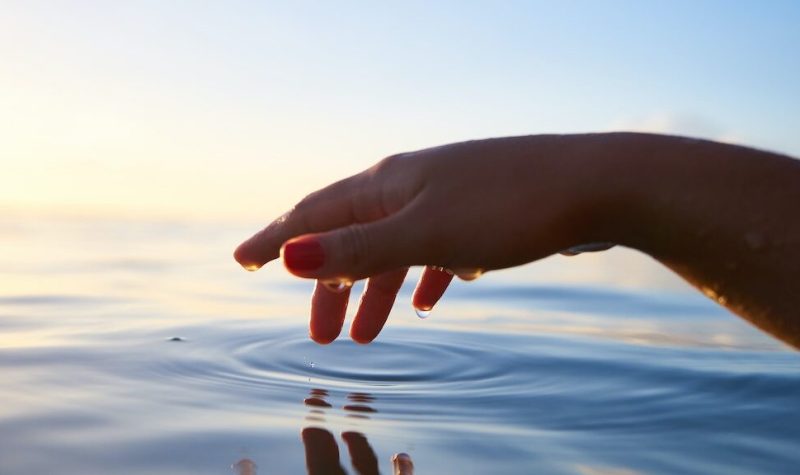A hand stretches out to touch an expanse of water